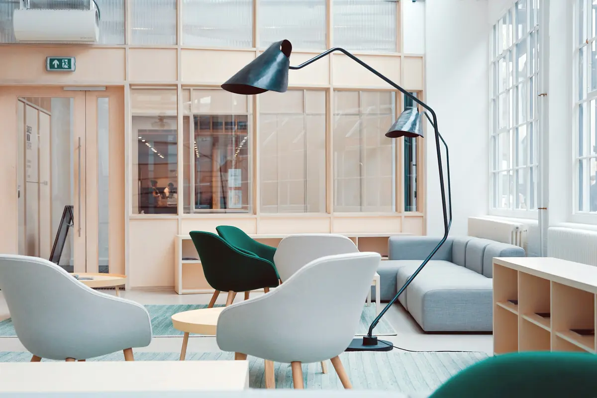 Sala de estúdio clara, com poltronas, divisórias de madeira e luz natural ampla.